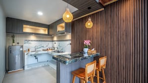 A modern kitchen with a marble backsplash, wooden paneling, and a bar area with two stools. - Hayana Villa Kintamani (Kintamani)