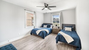Une chambre avec deux lits, un ventilateur de plafond et de grandes fenêtres.