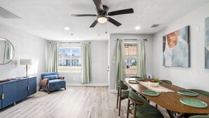 Un coin repas avec une table en bois, des chaises vertes et un ventilateur de plafond.