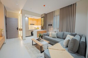 Una sala de estar moderna con un sofá gris, una mesa de centro de madera y una cocina al fondo.