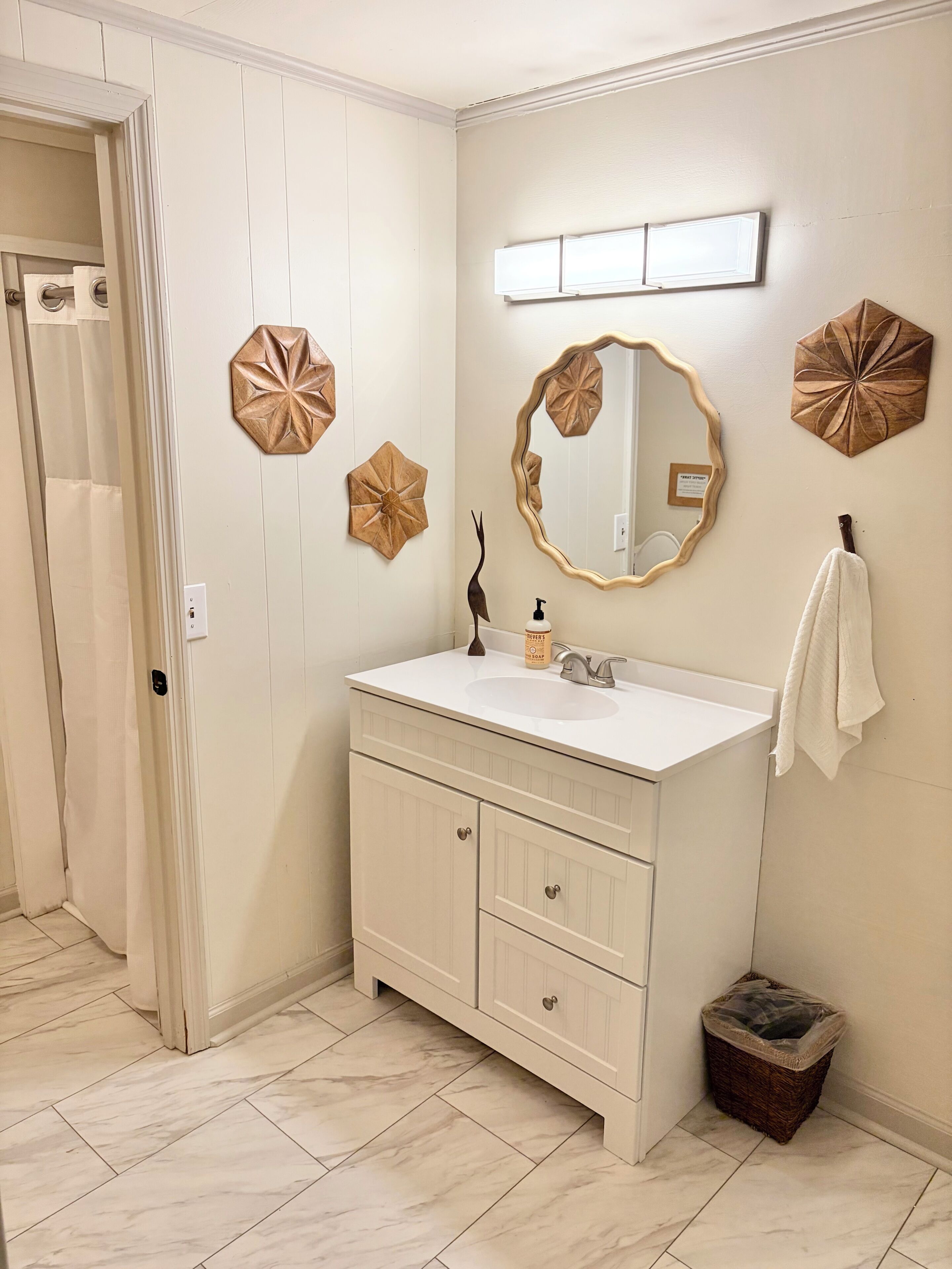A bathroom with a white vanity, a mirror, decorative wall art, a towel rack, and a trash bin.