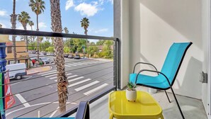 Ein Balkon mit Blick auf eine Straße, ein blauer Stuhl, ein gelber Tisch und ein Blumentopf.