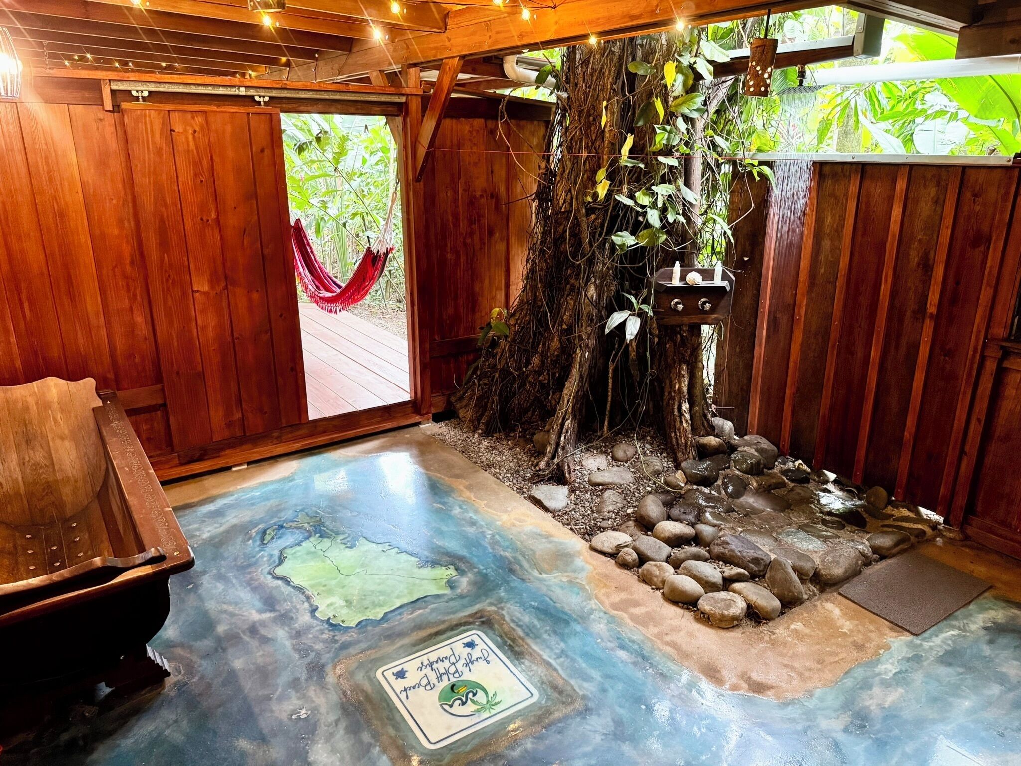 Un interior de madera con una hamaca, un tronco de árbol y una pequeña cascada.