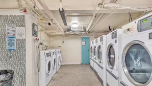 Un cuarto de lavandería con varias lavadoras, un bote de basura y una puerta azul.