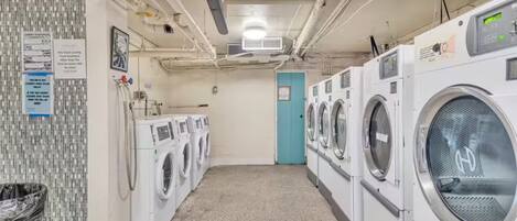 A laundry facility with multiple washing machines, a trash bin, and a blue door.