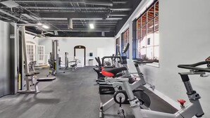 Un gimnasio con diversos equipos de ejercicio, incluyendo cintas de correr y máquinas de pesas, y un amplio ventanal que proporciona luz natural.