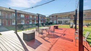 Un patio con mobiliario exterior, una terraza de madera y un edificio de ladrillo al fondo.