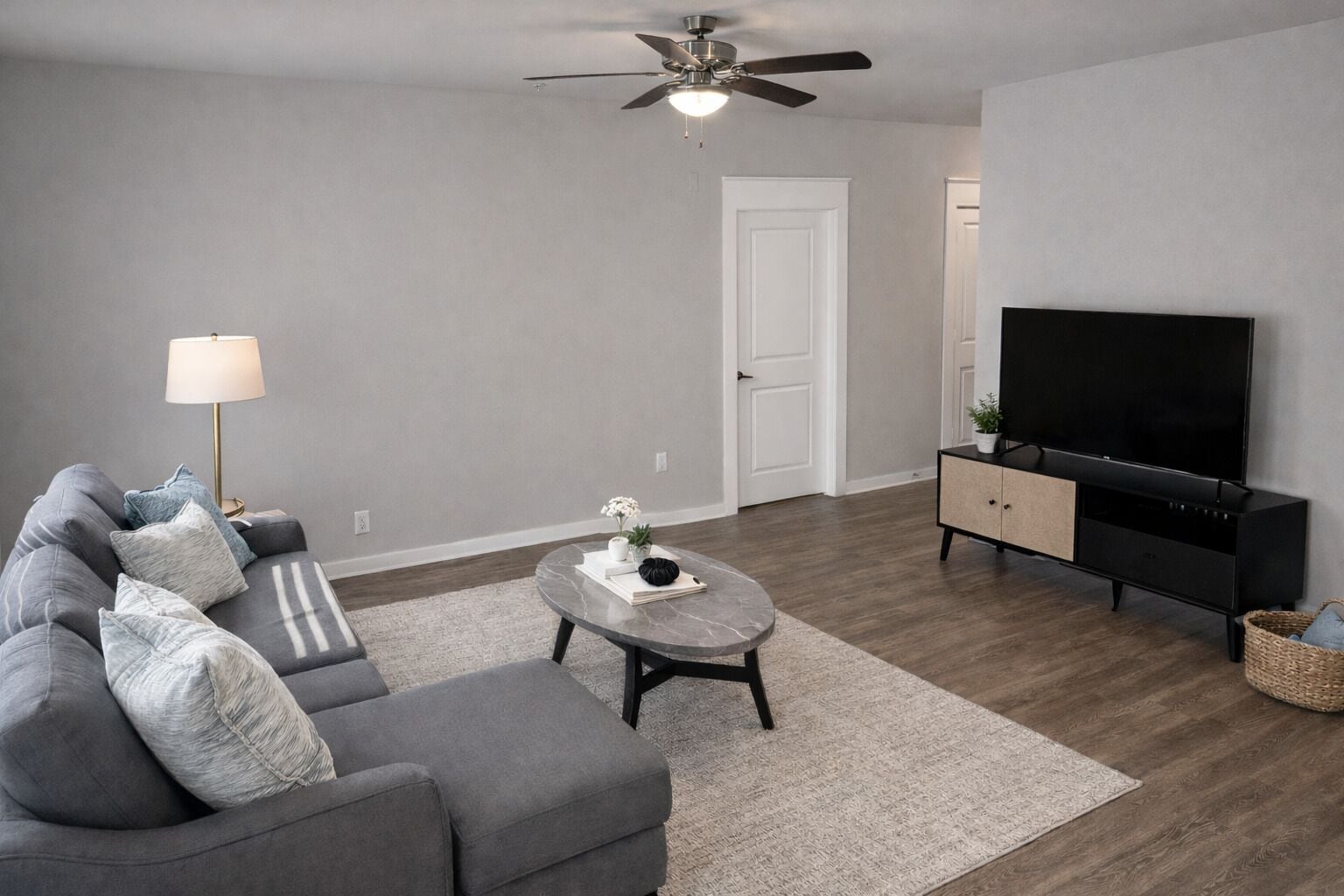 A modern living room with a grey sofa, a coffee table, a TV stand, and a ceiling fan.