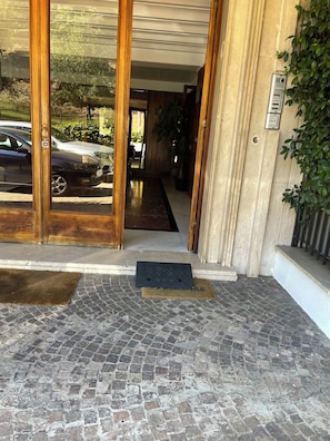 A hotel entrance with a cobblestone pathway, wooden doors, and a potted plant. - COZY HOUSE 5 MINUTES FROM SAN PIETRO INSIDE A GREEN AND QUIET RESIDENCE (Roma)