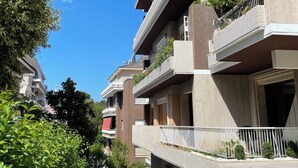 Un edificio residencial de varios pisos con balcones, un sendero estrecho y abundante vegetación.