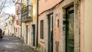 A narrow cobblestone street lined with historic buildings, featuring balconies with potted plants, green doors, and a visible fire alarm sign. - Alfama Tiny by Homing (Lisbon)