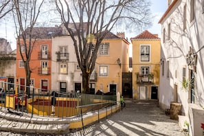 A cobblestone street with colorful buildings, a playground, and a tree in the center. - Alfama Tiny by Homing (Lisbon)