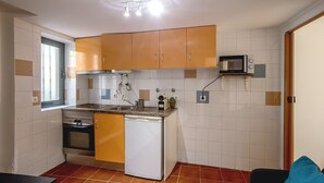A compact kitchen with a built-in oven, a microwave, and a dishwasher. There is a window providing natural light and a small countertop with a sink. - Alfama Tiny by Homing (Lisbon)