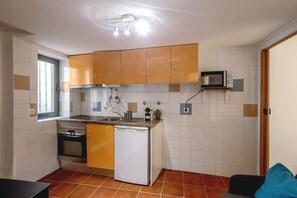 A compact kitchen with a built-in oven, a microwave, and a dishwasher. There is a window providing natural light and a small countertop with a sink. - Alfama Tiny by Homing (Lisbon)