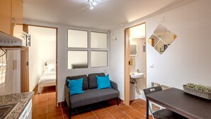 A compact living space with a kitchenette, a sofa with blue cushions, a dining table, and a small bathroom. - Alfama Tiny by Homing (Lisbon)