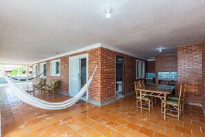A spacious patio with a hammock, a dining area with a table and chairs, and a TV mounted on the brick wall.