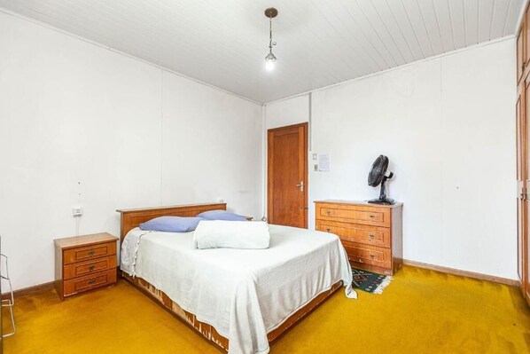 A bedroom with a bed, wooden dresser, and a mirror.