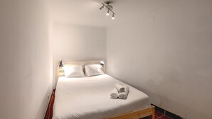 Een enkel bed met houten frame, witte beddengoed en twee opgerolde handdoeken op het bed.