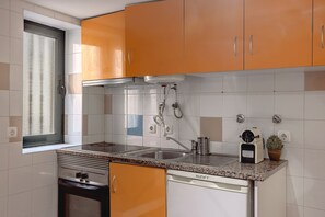 Eine Küche mit orangenen Schränken, einem Edelstahlherd, einer Spülmaschine und einem Fenster mit Vorhang.