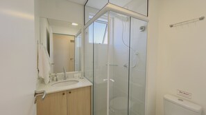 A modern bathroom with a glass shower enclosure, a sink with a mirror, and a toilet. - Solarium Beach Club - Apartamento T1.307 (Itapoá)