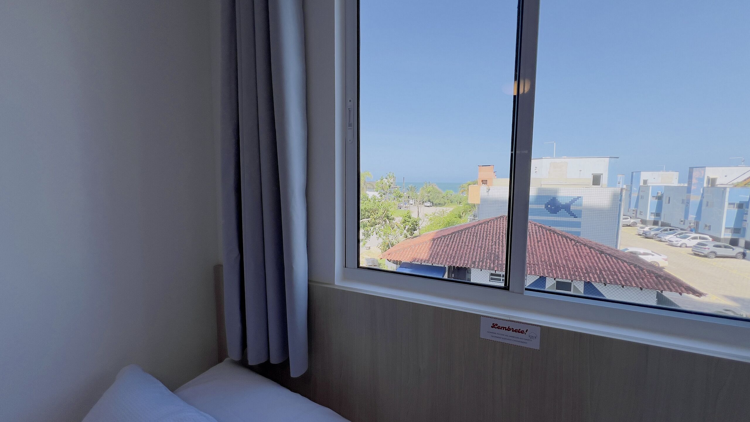 A hotel room with a large window offering a view of a parking lot and buildings.