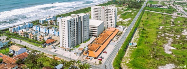 An aerial view of a coastal hotel area with multiple buildings, including high-rise and low-rise structures, near the beach.