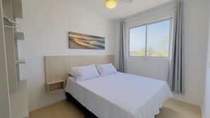 A neatly arranged bedroom with a bed, a nightstand, a painting, and a window with curtains.