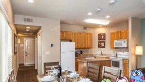 A modern kitchen with wooden cabinets, a microwave, and a stove. There is a dining area with a table set for four.