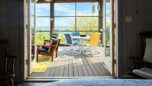 Een open deur die leidt naar een terras met tuinmeubilair en uitzicht op de oceaan.