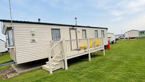A single-story mobile home with a front porch and a small set of stairs leading to the entrance. - Singh&leite Family L6 (Clacton-on-Sea)