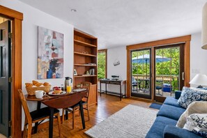 Ein gemütliches Wohnzimmer mit Essbereich, einer Bücherwand und Blick ins Freie durch große Schiebeglasfenster.