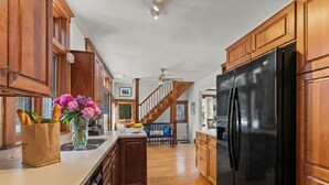 Una cucina con mobili in legno, un frigorifero nero e una scala in legno che conduce a un altro piano.