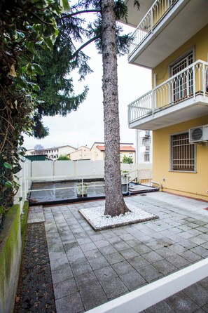 Un patio con un árbol, una pequeña fuente y un edificio amarillo con balcón.