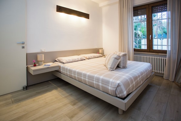 Un dormitorio con cama, mesita de noche, lámpara y ventana con cortinas.