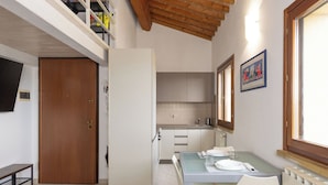 Een compacte keuken met een eethoek, een slaapkamer op een entresol met balkon en een groot raam.