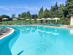 A clear blue pool with green lounge chairs and umbrellas, surrounded by trees. - Cinquantina by Interhome (Cecina)