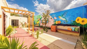 A garden patio with a wooden pergola, a colorful mural, a bench, and a pathway. - Casa Kolibrí - 8 Bedrooms + Pool + Outdoor Kitchen + Coworking (Mérida)