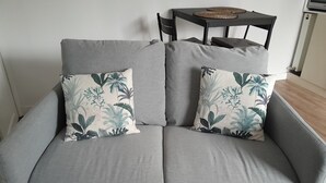 En grå sofa med to puder med blomstermønster og et lille bord med vævede bordskåner.