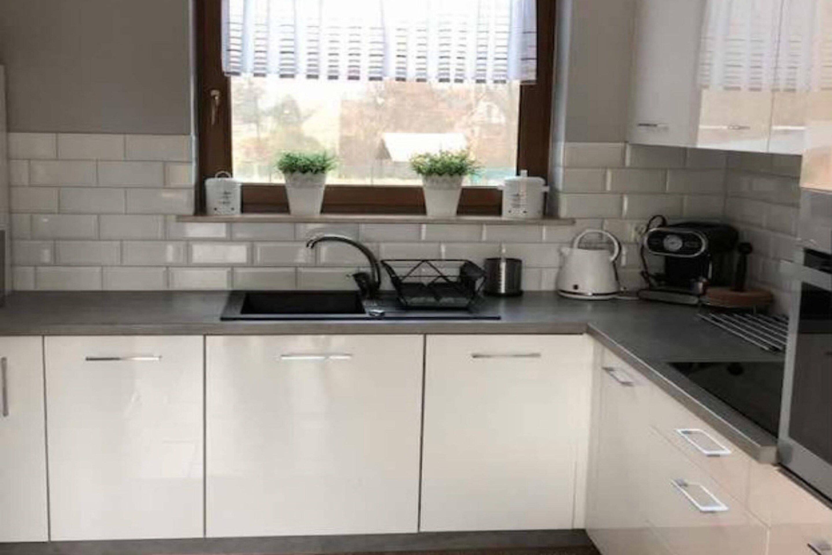 A modern kitchen with white cabinetry, a stainless steel sink, and a window with blinds.