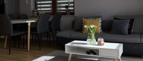 A modern living room with a grey sofa, a white coffee table, and a dining area with chairs and a table.