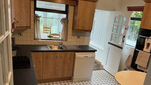 Een keuken met houten kastjes, een zwart aanrecht, een witte vaatwasser en een vloer met een patroon.