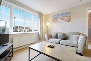 A living room with a sofa, a coffee table, a TV, and a window with a view of houses. - 4 Bedroom Comfort Stylish Home in Central Barnsley (Monk Bretton)