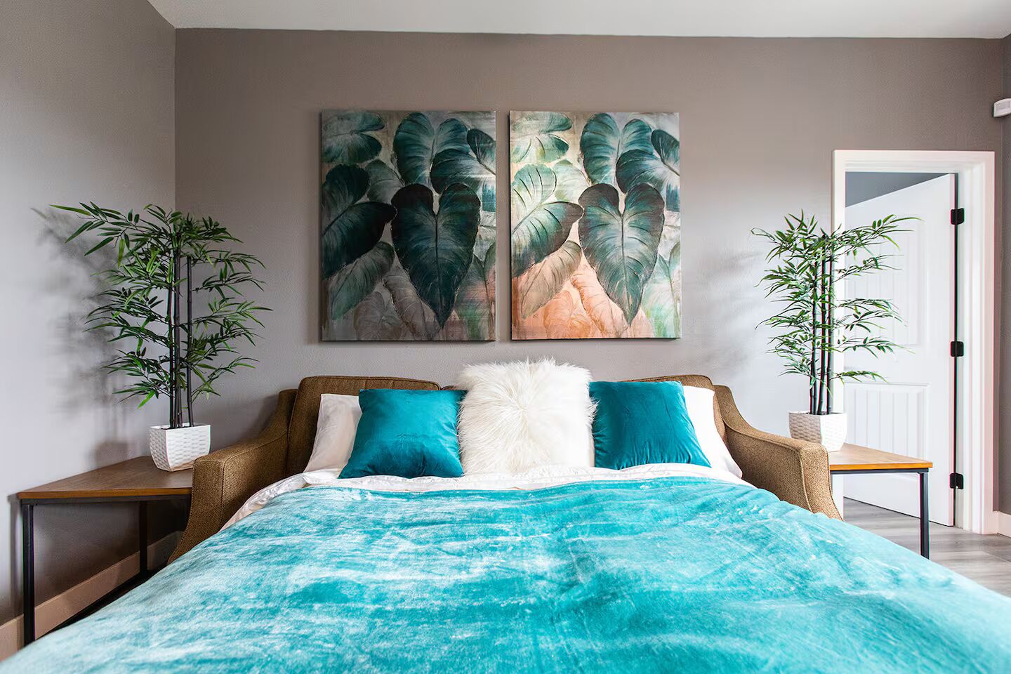A bedroom with a bed, two nightstands, two potted plants, and two wall art pieces.