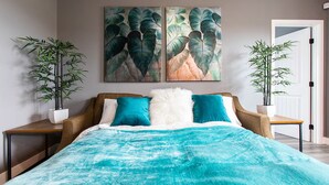 Quarto com cama, duas mesas de cabeceira, duas plantas em vasos e duas obras de arte nas paredes.
