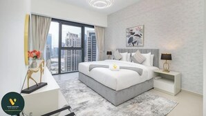 A modern bedroom with a large bed, bedside lamps, a city view, and a decorative wall piece. - Vogue | Act One near Burj Khalifa | Dubai Mall (Dubai)