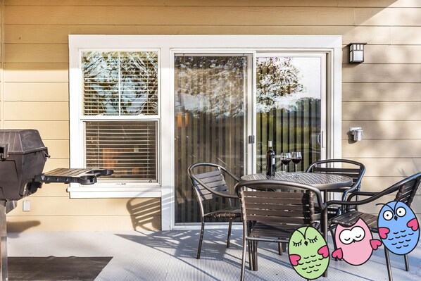 A patio with a grill, a table, and chairs, and a sliding glass door.