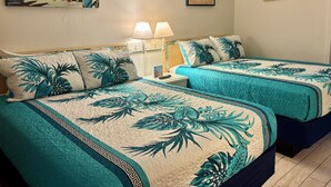 Quarto de hotel com duas camas, cada uma com roupa de cama floral em tons de verde-água e branco, um quadro com tema tropical na parede e uma pequena fotografia emoldurada.