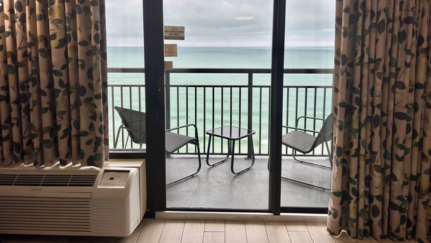 Quarto com vista para o mar, placa proibindo fumar e janela com cortinas.