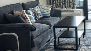 Uma sala de estar moderna com um sofá cinzento, almofadas decorativas, uma mesa de centro preta e um tapete estampado.