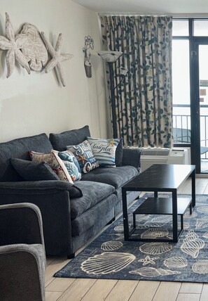 Ein modernes Wohnzimmer mit einem grauen Sofa, dekorativen Kissen, einem schwarzen Couchtisch und einem gemusterten Teppich.